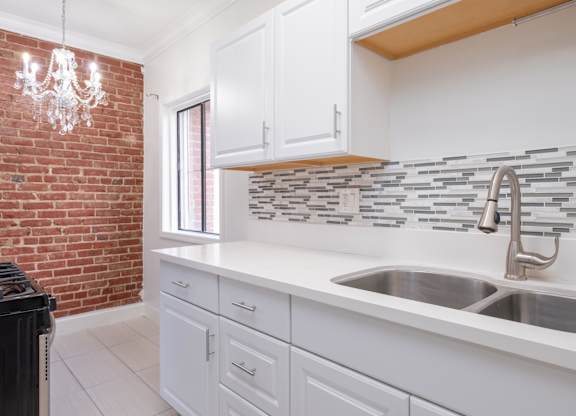 A kitchen with white cabinets and a brick wall at Mariposa Willows Apartments, Los Angeles