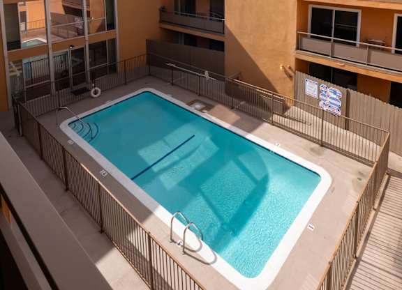 A pool on a balcony with a building and palm trees in the background at Menlo Terrace Apartments, Los Angeles, California