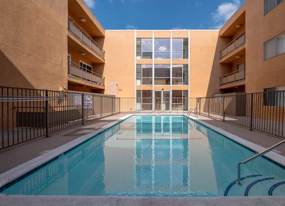A swimming pool in front of a tan building with black railings at Menlo Terrace Apartments, Los Angeles, CA