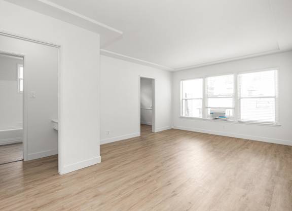 A white room with wooden floors and a window.at Normandie Grove, Los Angeles, CA 