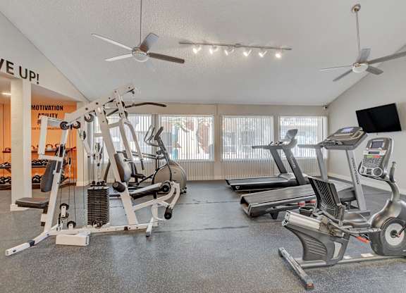 A gym with a variety of equipment including treadmills, elliptical machines, and a weight bench.