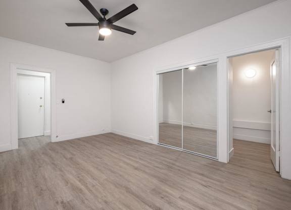 A room with a ceiling fan and light, wooden floors, and a glass door at Westmore Manor Apartments, California