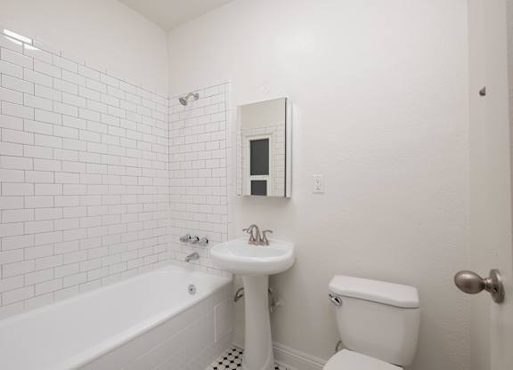 A white bathroom with a tub, toilet, and sink at Westmore Manor Apartments, Los Angeles, California