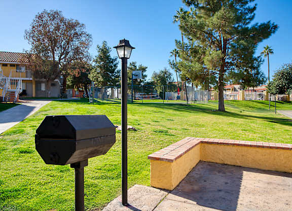 A black mailbox sits on a pole next to a brick bench in a sunny park.
