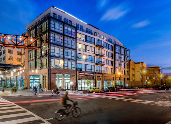 A cyclist is crossing the street in front of a modern multi-story building.
