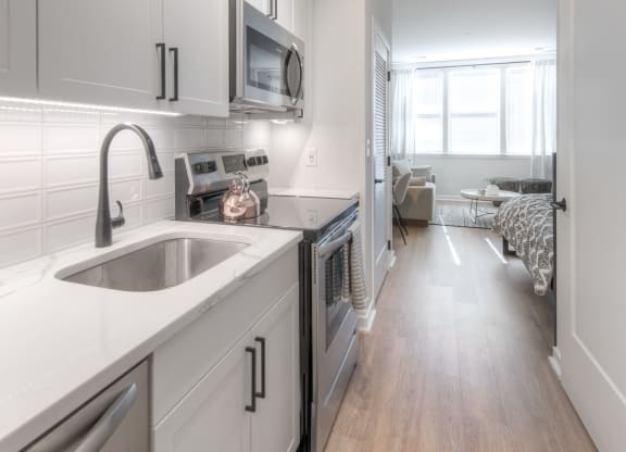 Galley kitchen with cupboards, sink, dishwasher, microwave, white cabinets, and a sink