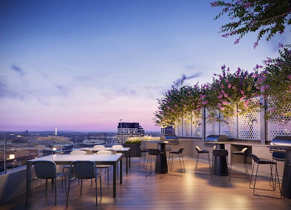 A balcony with a table and chairs overlooking a cityscape at dusk.