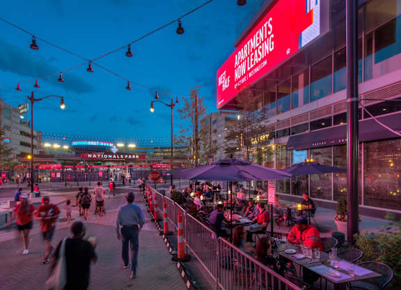 A busy outdoor bar scene with people walking and sitting at tables.