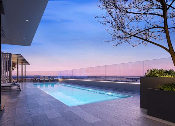 A modern outdoor pool area with a tree and a fence in the background.