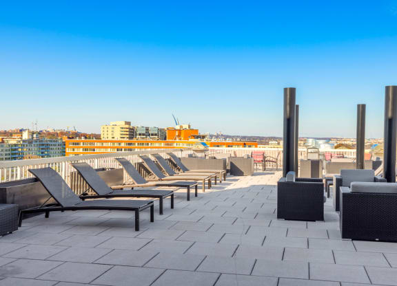 a row of lounge chairs on a rooftop patio overlooking the city