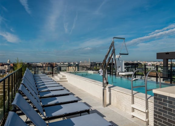 a rooftop pool with lounge chairs and a city in the background