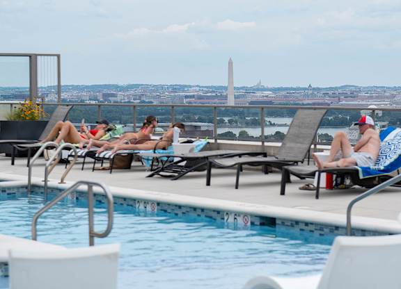 People sunbathing by a pool with a view of the Washington Monument in the distance.