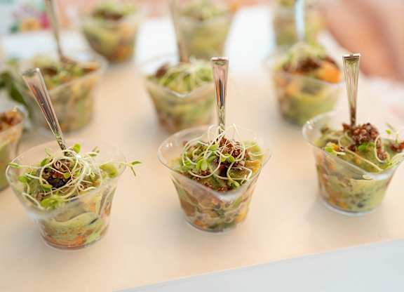 A row of clear cups filled with salad and topped with sprouts.