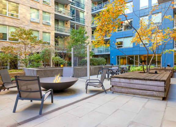 an outdoor patio with chairs and a fire pit in front of an apartment building