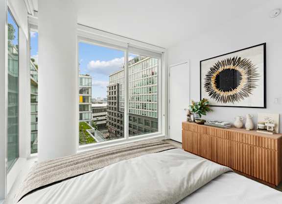 A bedroom with a large window overlooking a cityscape.