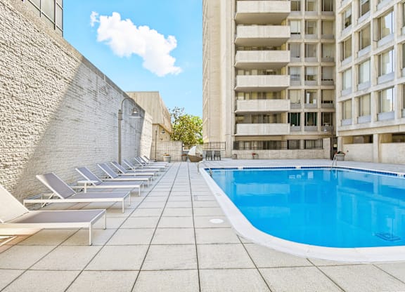 A pool surrounded by sun loungers and a brick wall.