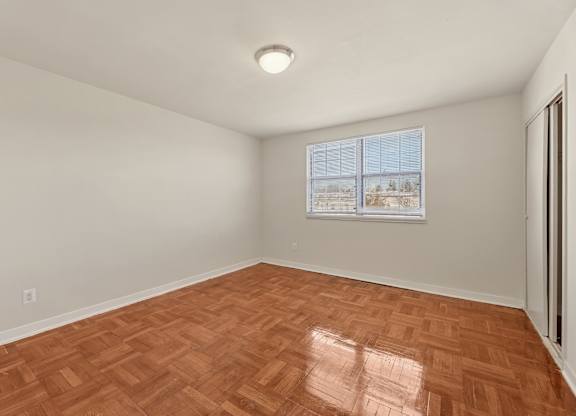 A room with a wooden floor and a window showing a view of trees outside.