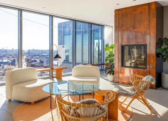 A modern living room with a glass table and chairs, a fireplace, and a view of the city.