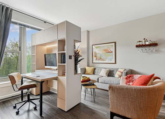 A room with a desk, a chair, a couch, and a shelf with decorative items.