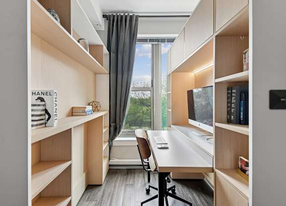 A room with a desk, a chair, and shelves with books and decorations.