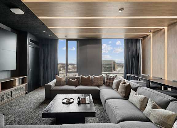 A modern living room with a large grey sofa and a coffee table in front of a large window.