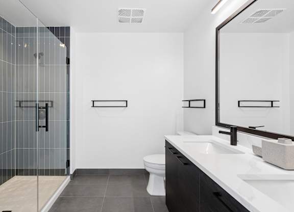 A modern bathroom with a walk-in shower, toilet, and double sinks.