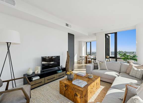 A living room with a white couch, a wooden coffee table, and a large window.