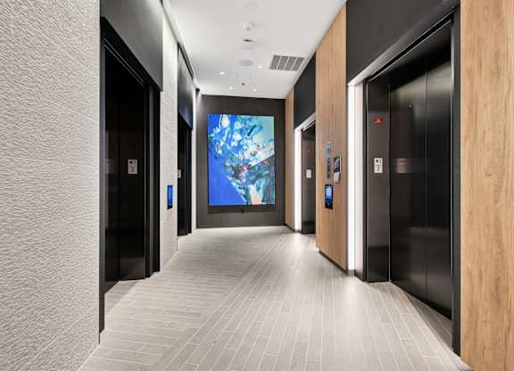 A hallway with a large screen on the wall and elevators on the side.