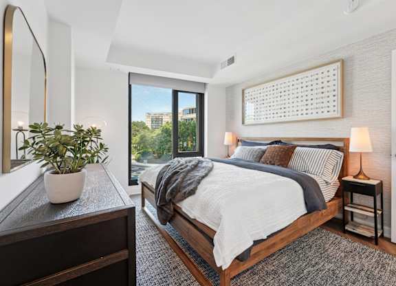 A bedroom with a large bed, a potted plant, and a mirror on the wall.
