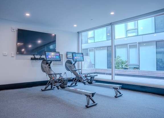 A room with a television, two exercise bikes, and a bench.