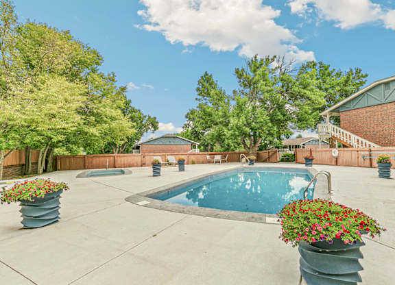 A pool surrounded by trees and concrete planters with flowers.