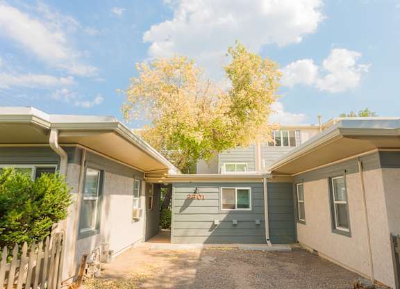 A house with a grey and white exterior and a tree with yellow leaves in the background.