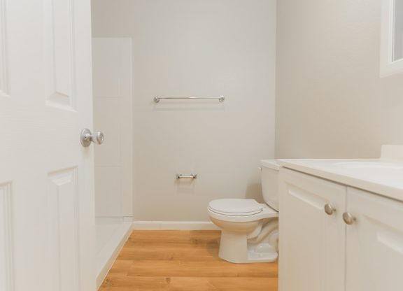 A white bathroom with a toilet, sink, and wooden floor.