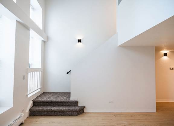 A staircase with a carpeted runner leads up to a white wall.