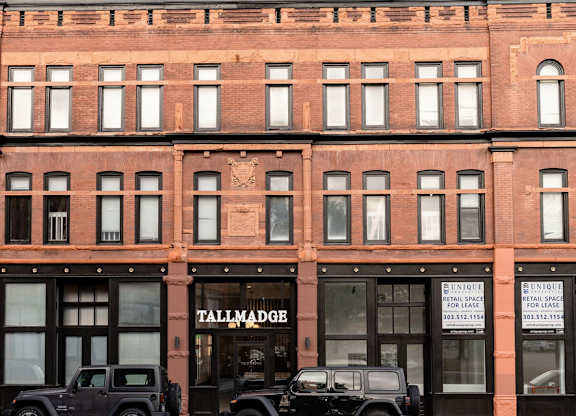 A tall red brick building with a black Jeep parked in front.