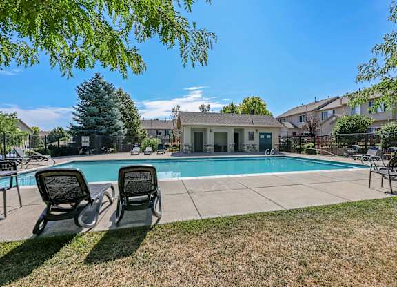 Two lounge chairs sit on the lawn in front of a pool and a house.
