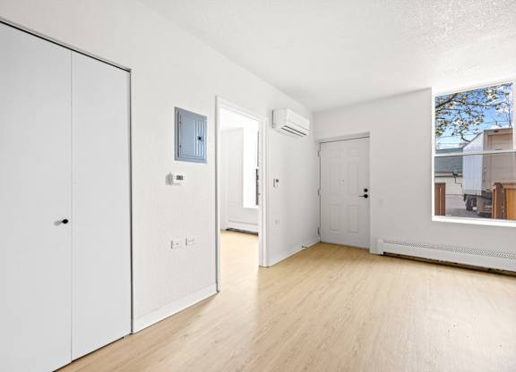 A white room with a wooden floor and a window showing a view of a building outside at Tallmadge Lofts in Denver, Colorado