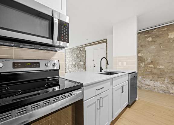 A kitchen with a black stove top oven and a black microwave above a white counter at Tallmadge Lofts in Denver, Colorado