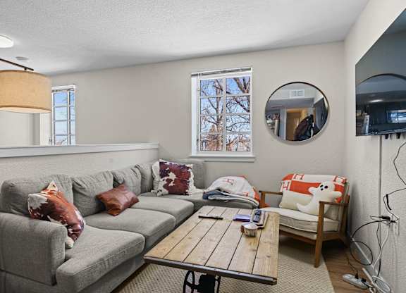 A living room with a grey couch, a wooden coffee table, and a round mirror on the wall.