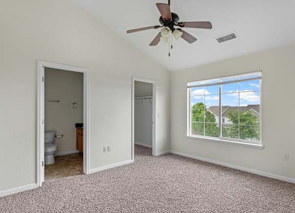 A room with a ceiling fan and a window overlooking a house.