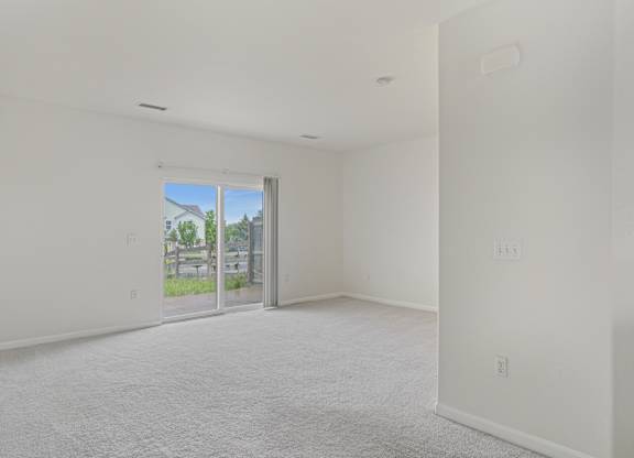 A large empty room with a sliding glass door leading to a patio.