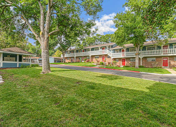 A tree stands in a grassy area in front of apartment buildings.