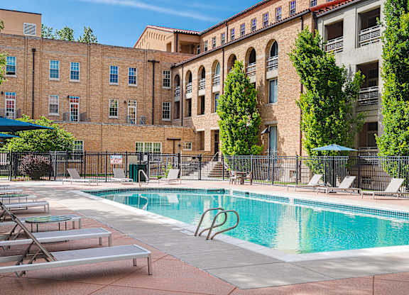 A pool surrounded by lounge chairs and trees in front of a building.