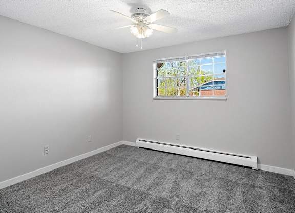 A room with a ceiling fan and a window with a view of a building outside.