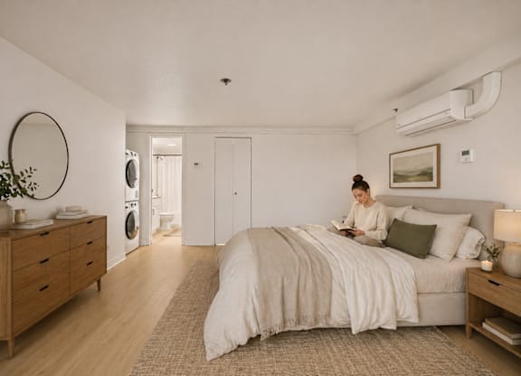 A woman is sitting on a bed in a room with wooden floors and furniture.