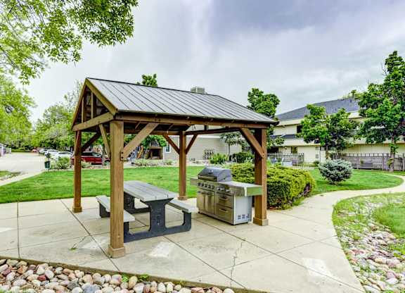 A wooden pavilion with a black roof and a picnic table in front of a grassy area.