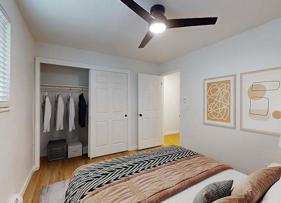 A bedroom with a bed, a ceiling fan, and a closet with clothes hanging.