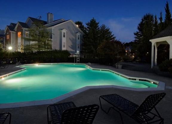 A pool surrounded by chairs and a house in the background.