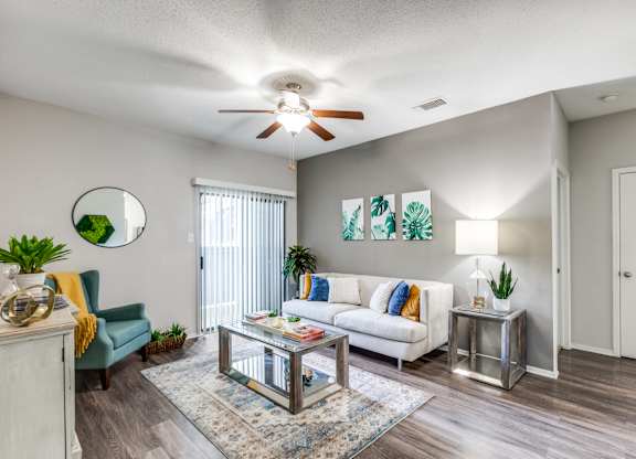 A living room with a white couch, a glass coffee table, and a ceiling fan.