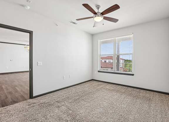 A room with a ceiling fan and a window overlooking a cityscape.